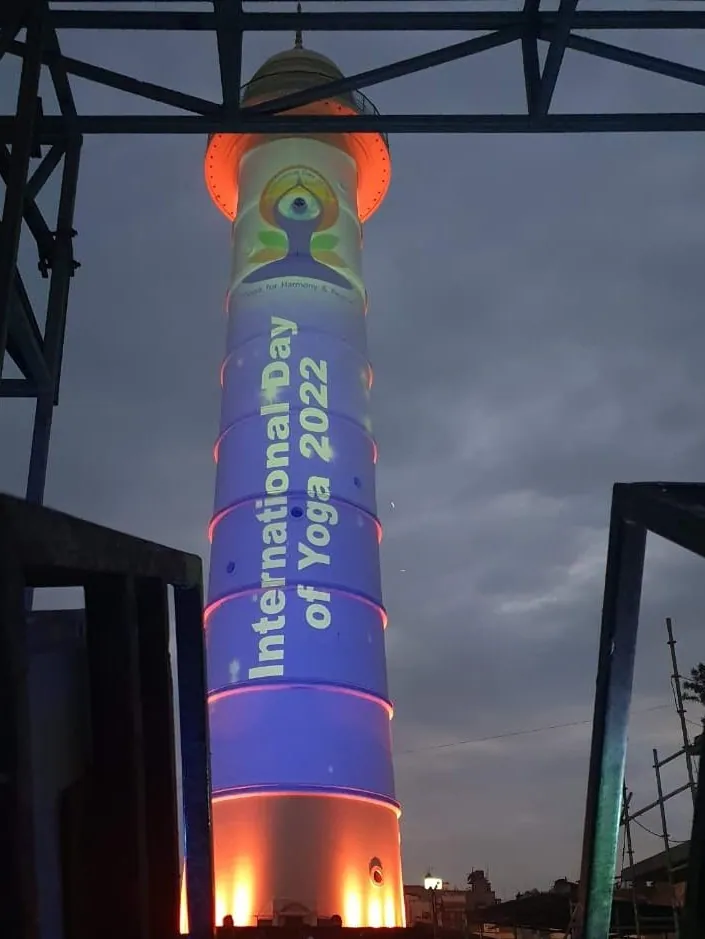 The tower in blue with the International Day of Yoga 2022 emblem and title projected down the shaft, seen between projector cages.