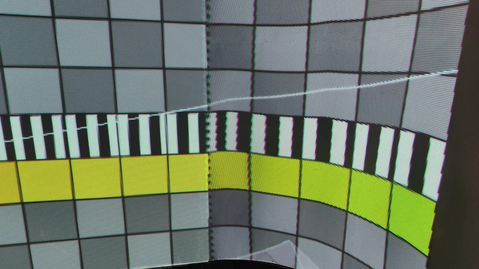 Close view of a test pattern of grey checks, black and white stripes and a yellow-green bar bending across the seam between two projectors.