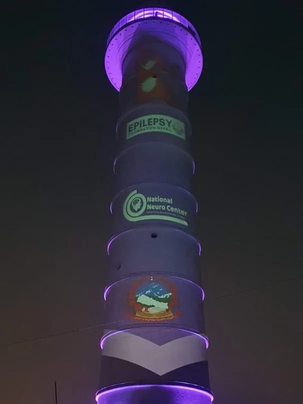 The tower lit purple with logos for Epilepsy Foundation Nepal, National Neuro Center and the Government of Nepal emblem.