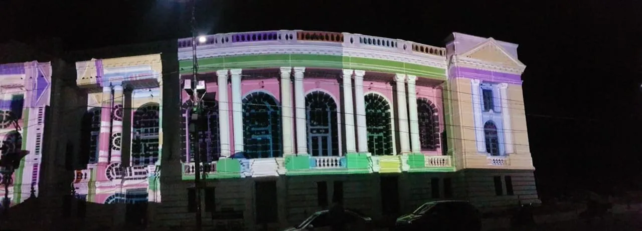 Night photograph of the curved corner of the building with the same colour-coded projection wrapping around its columns and balustrade.