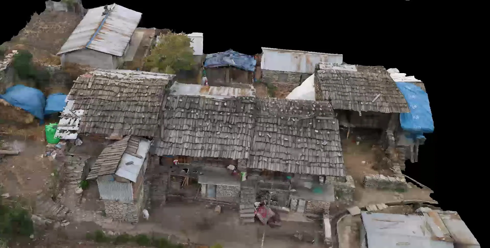 Aerial three-quarter view of the Block B model: a cluster of stone houses with shingle roofs, blue tarpaulins and terraced ground.