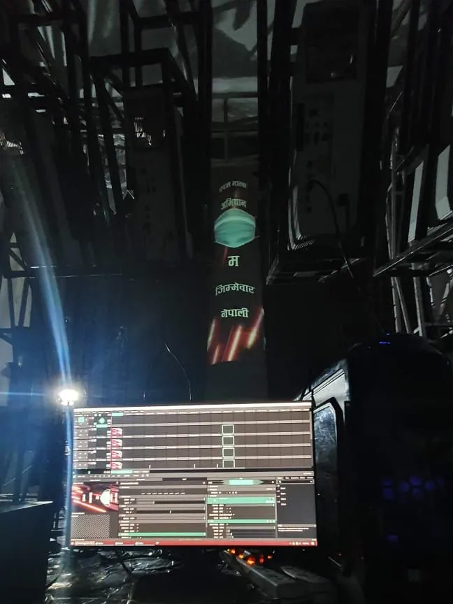 A monitor showing a timeline and clip grid in front of the tower, which carries the mask campaign in the background.