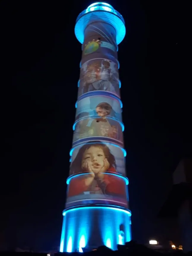 The tower in blue light with photographs of children projected in bands down the shaft.