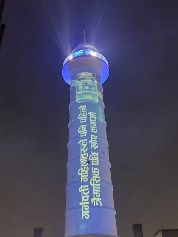 The tower in blue with a COVID-19 vaccine bottle and a Nepali line about pregnant women getting their first vaccine dose.
