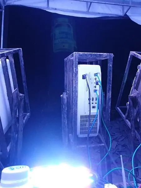 Four projectors seen from behind in steel cages inside the tent, cabled together, with a vaccine bottle graphic on the tower beyond.