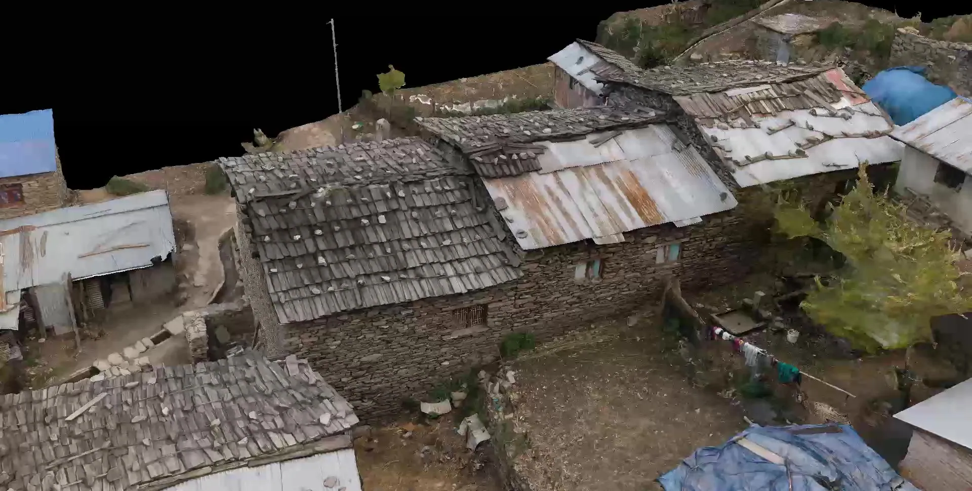 Aerial view of the Gatlang model showing shingle and metal roofs of stone houses, blue tarpaulins and a path between the buildings.