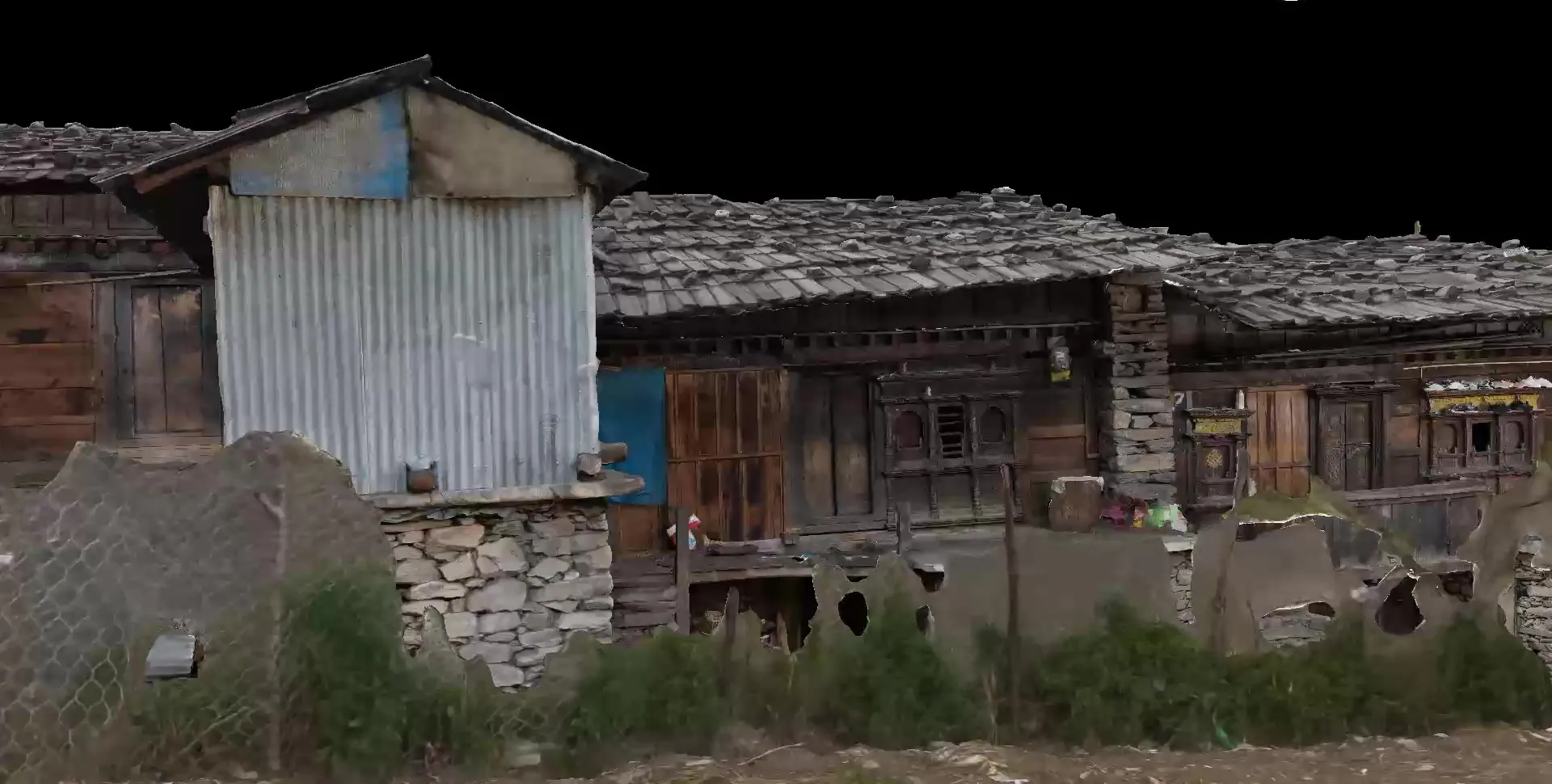 View of the Gatlang model along a row of timber houses with wooden-shingle roofs, a corrugated-metal gable and stone footings.